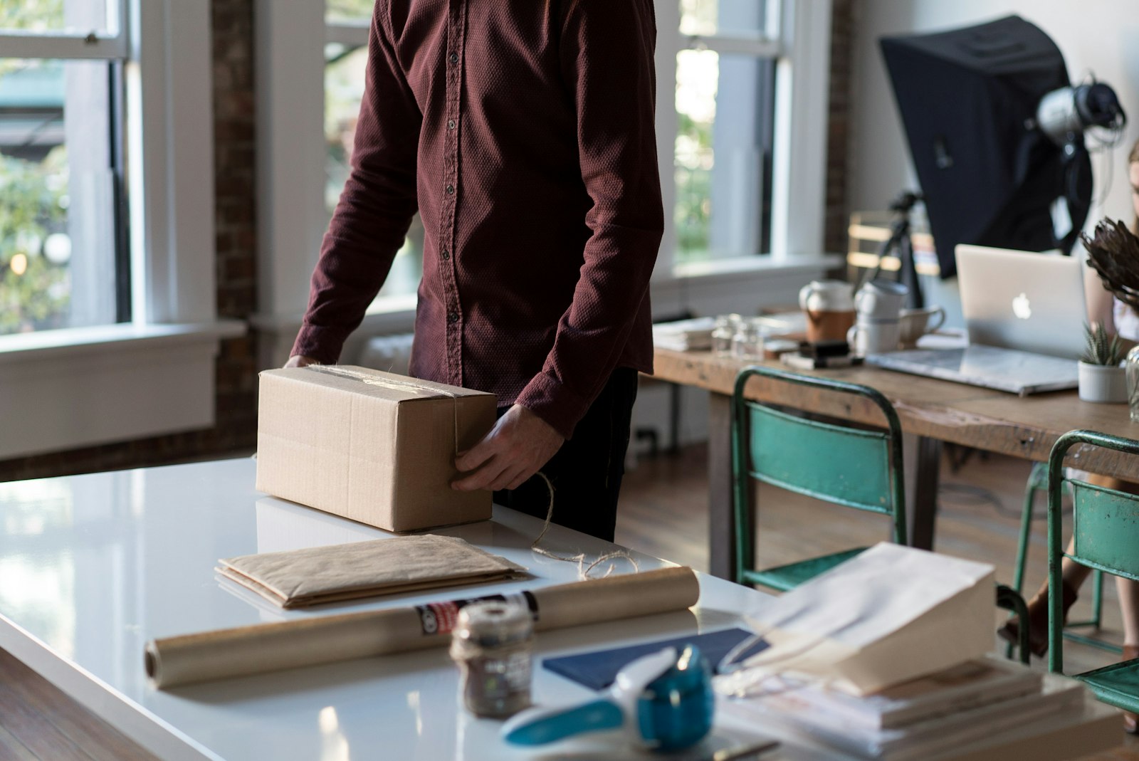 A person holding a cardboard box on a table, ready to ship an online order.